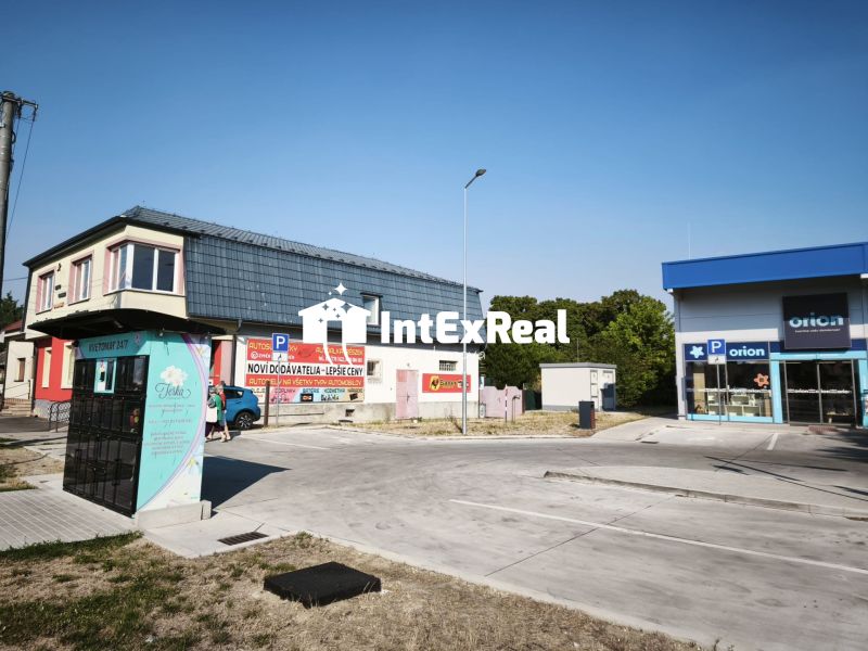 Obchodní prostory na ulici SNP v Šaľe s parkovištěm a reklamními nápisy.