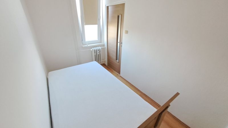 Ložnice s bílými stěnami a podlahou s dřevěným dekorem ve 2pokojovém bytě.