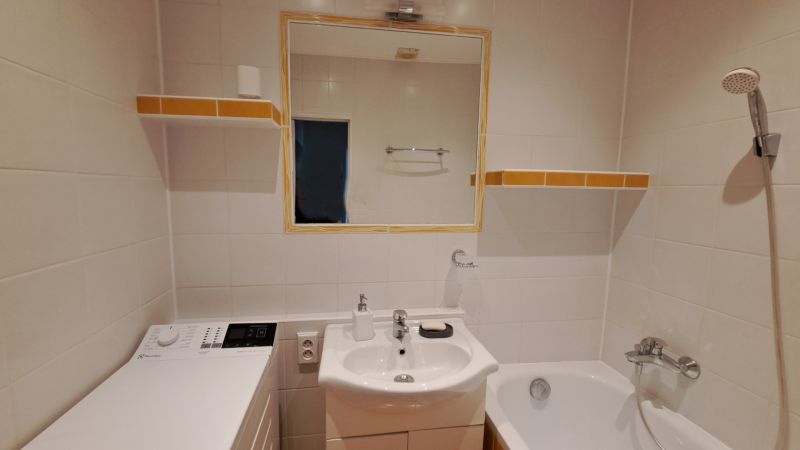 Koupelna s umyvadlem, zrcadlem, pračkou a vanou ve 2pokojovém bytě.
