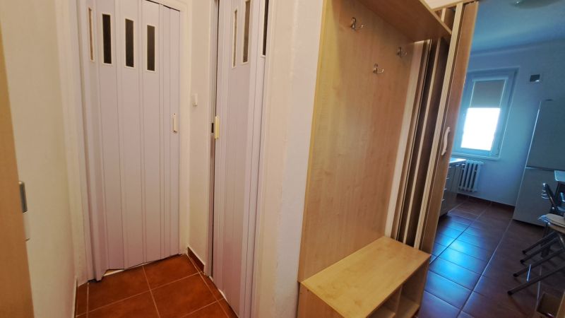 Vstup s hnědou dlažbou, šatníkovou skříní a posuvnými dveřmi v 2-pokojovém bytě.