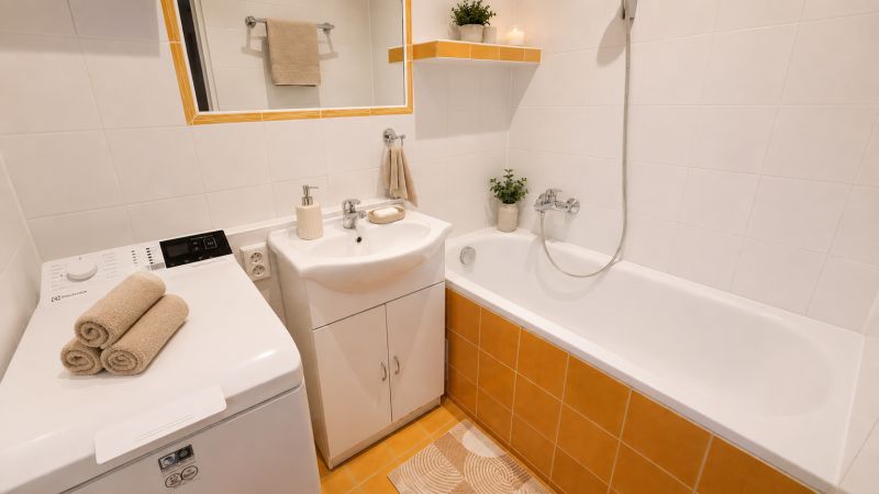 Koupelna s vanou, umyvadlem, pračkou a dekorativními ručníky v 2pokojovém bytě.