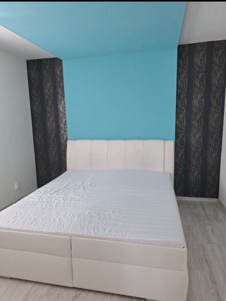 Světlá ložnice s bílou postelí a modrou stěnou v třípokojovém bytě.