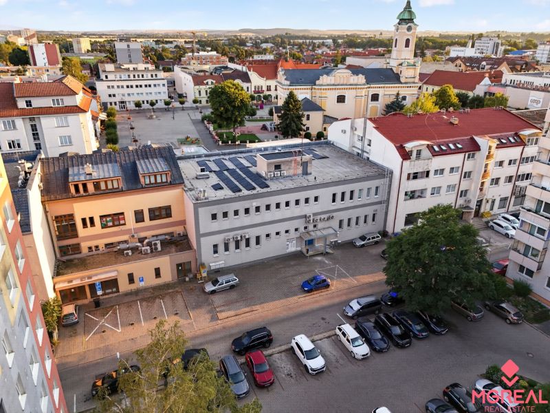 Pohled na M.R. Štefánika v Topoľčanech s obchodními prostory a kostelem v pozadí.