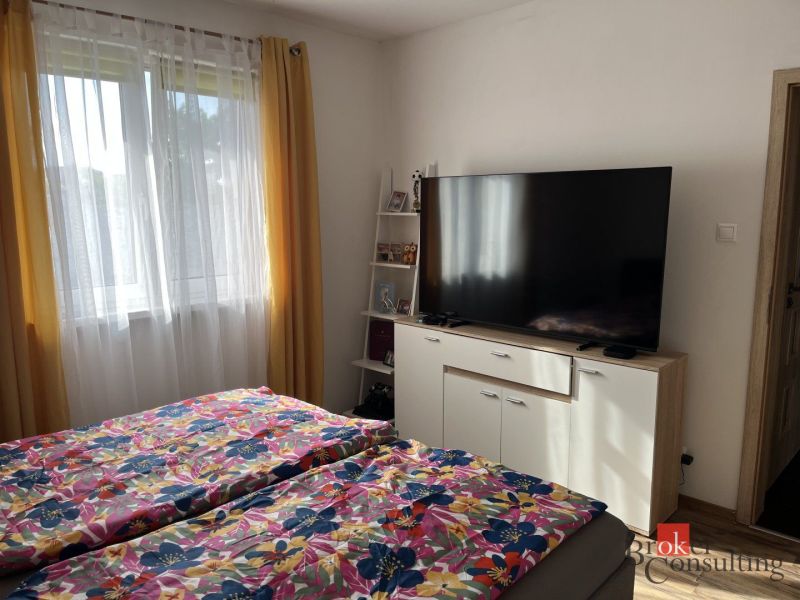 Ložnice v rodinném domě s TV, květinové povlečení, žluté závěsy, okno.