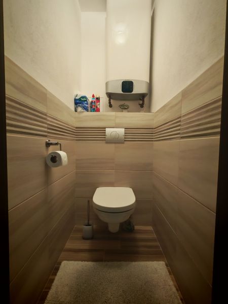 Koupelna v 2-pokojovém bytě s toaletou, obložená kachličkami na stěnách a podlaze s dřevěným dekorem.