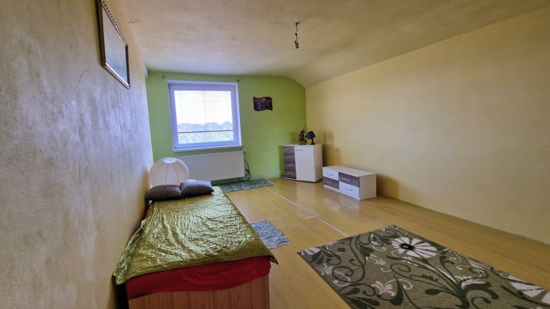 Jednoduchý pokoj s postelí, světlými stěnami a podlahou s dřevěným dekorem.