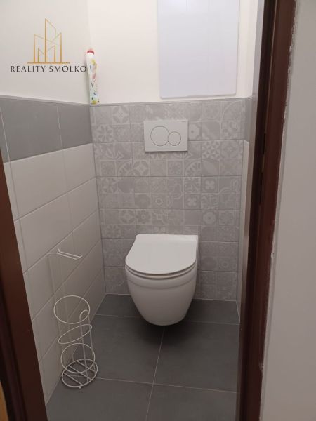 Toaleta v 2-pokojovém bytě s dekorativními obklady stěn a šedou podlahou.