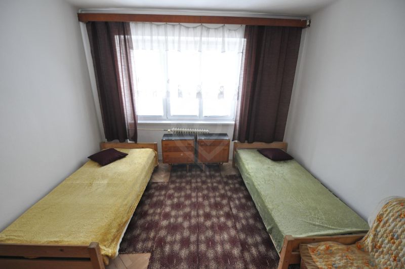 Ložnice se dvěma jednolůžky, kobercem a oknem v 2-pokojovém bytě.