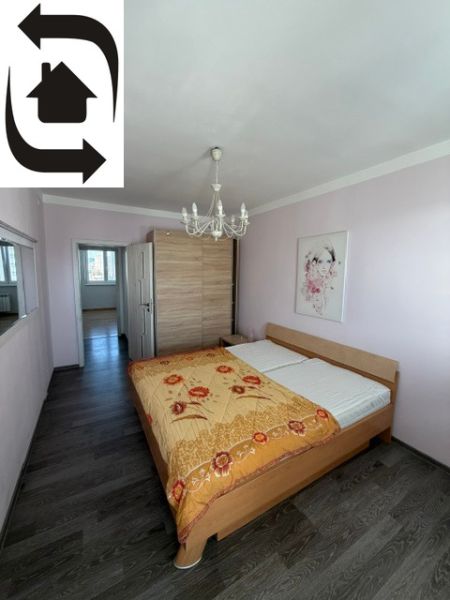 Ložnice v 3-pokojovém bytě s postelí, lustrem a podlahou s dřevěným dekorem.