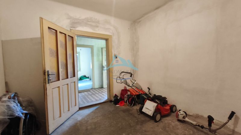 Interiér rodinného domu s otevřenými dveřmi, sekačkou a nářadím na podlaze.