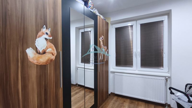 Skříň s dekoracemi zvířat v rodinném domě, dřevěná podlaha, radiátor pod oknem s roletami.