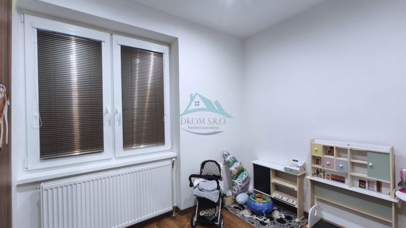 Dětský pokoj v rodinném domě s hračkami, kočárkem a podlahou s dřevěným dekorem.