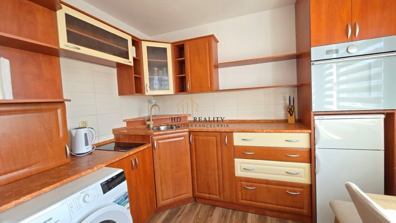 Kuchyně s dřevěným dekorem v 1-pokojovém bytě, vybavená pračkou a lednicí.