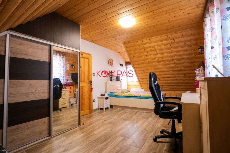 Podkrovní pokoj s dřevěným obkladem stropu, postelí, skříní a podlahou s dřevěným dekorem.