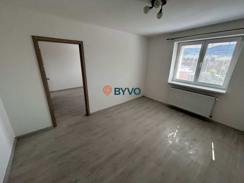 Pokoj s podlahou s dřevěným dekorem, bílými stěnami a velkým oknem ve 3-pokojovém bytě.