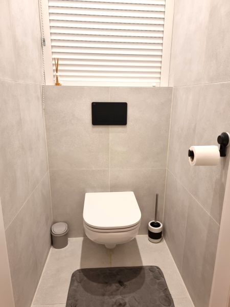 Koupelna v 2-pokojovém bytě s moderním závěsným WC na světlých dlaždicích.