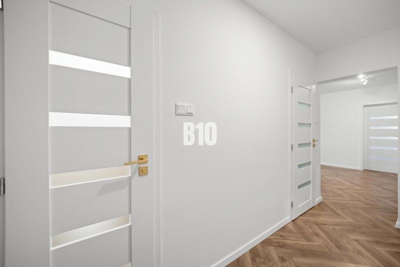 Bílý interiér 3pokojového bytu s podlahou s dřevěným dekorem a elegantními dveřmi.