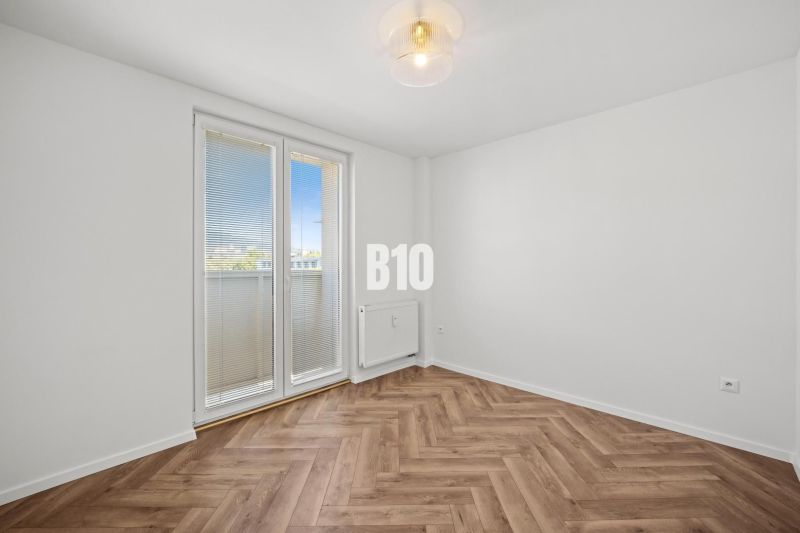 Prázdný pokoj s podlahou s dřevěným dekorem a balkónovými dveřmi ve 3-pokojovém bytě.