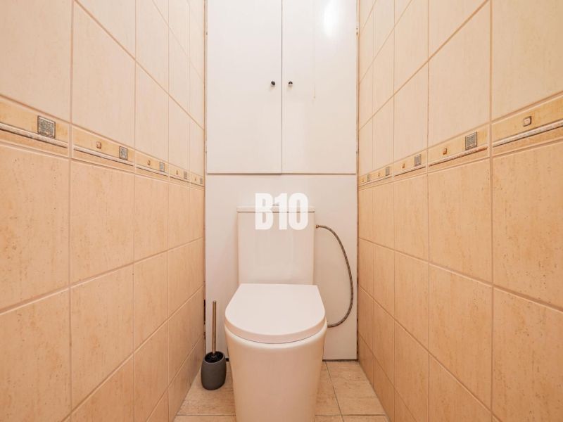 Toaleta s béžovým obkladem v 1-pokojovém bytě, praktický design a úložný prostor.