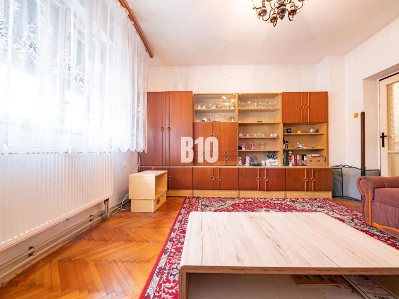 Obývací pokoj s přehlednou vitrínou, podlahou s dřevěným dekorem a červeným kobercem v rodinném domě.