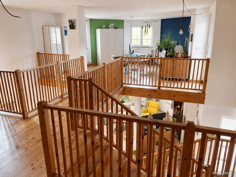 Interiér rodinného domu s podlahou s dřevěným dekorem a dřevěným zábradlím.