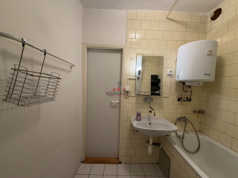 Koupelna v 3-pokojovém bytě s umyvadlem, vanou a ohřívačem vody na stěně.