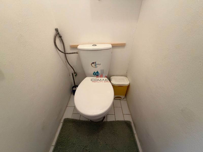Toaleta 3-pokojového bytu s bílými stěnami a dlaždicemi.