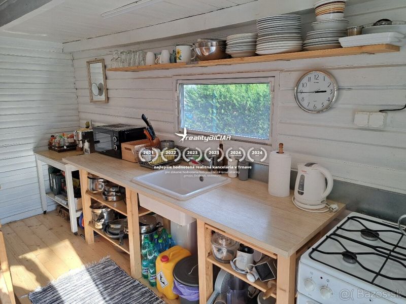Kuchyně v chatě s policemi, pultem a podlahou s dřevěným dekorem.