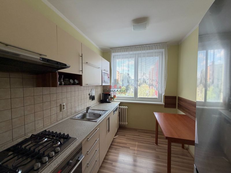 Kuchyně ve 3-pokojovém bytě s podlahou s dřevěným dekorem a jídelním stolem.