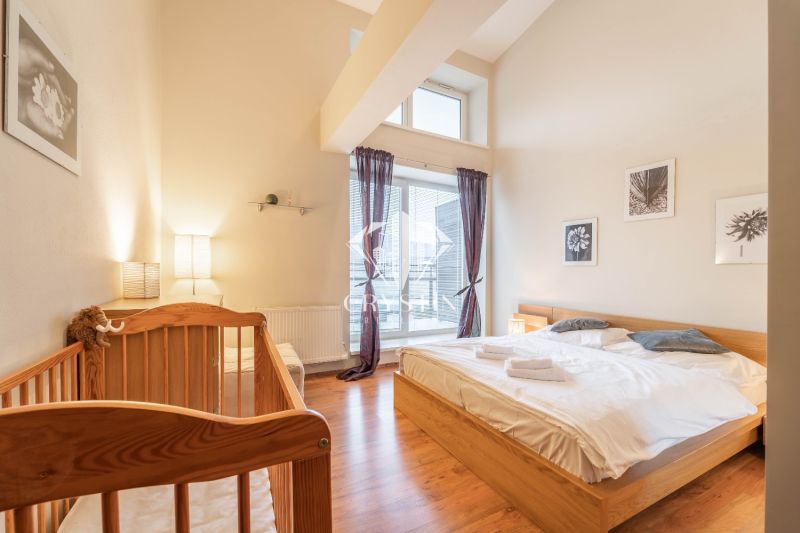 Světlá ložnice v rekreačním apartmánu s dětskou postýlkou a podlahou s dřevěným dekorem.