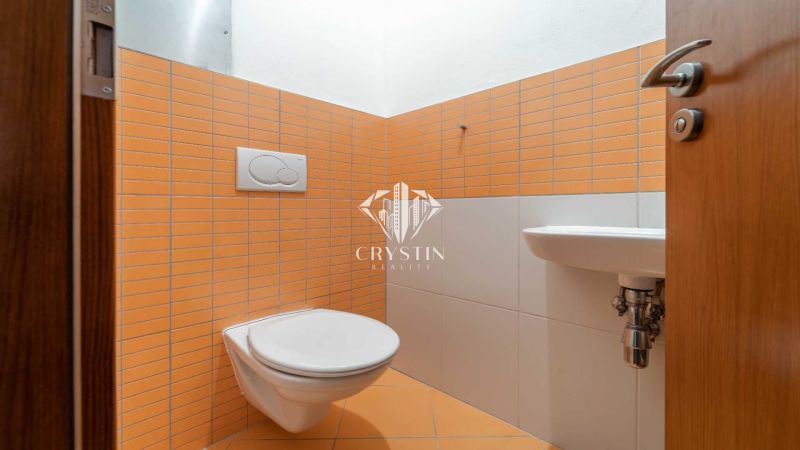 Koupelna v Rekreačním apartmánu s oranžovými obklady a závěsnou toaletou.