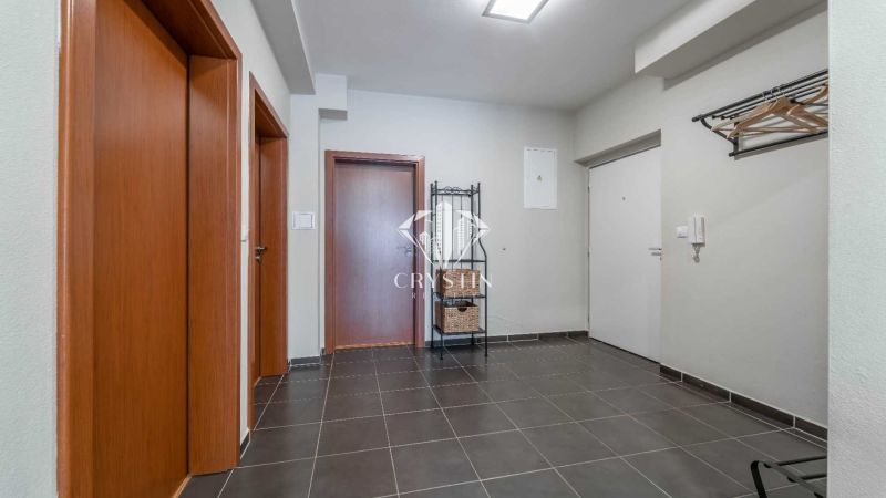 Vstupní hala rekreačního apartmánu s tmavou dlažbou, dřevěnými dveřmi a věšákem.