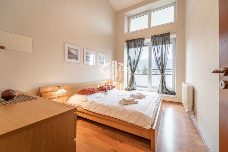 Světlá ložnice s manželskou postelí a podlahou s dřevěným dekorem v rekreačním apartmánu.