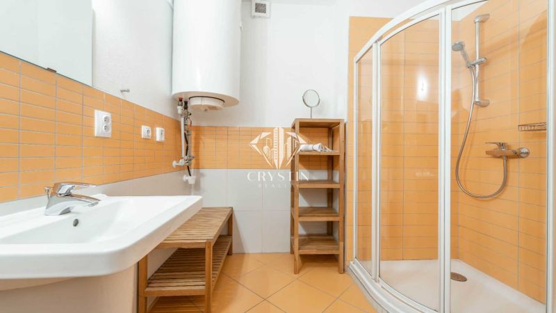 Koupelna s oranžovými obklady, sprchovým koutem a umyvadlem v rekreačním apartmánu.