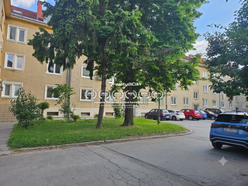 Parkoviště u 3pokojových bytů na Studentské ulici v Trnavě, obklopené zelení a stromy.