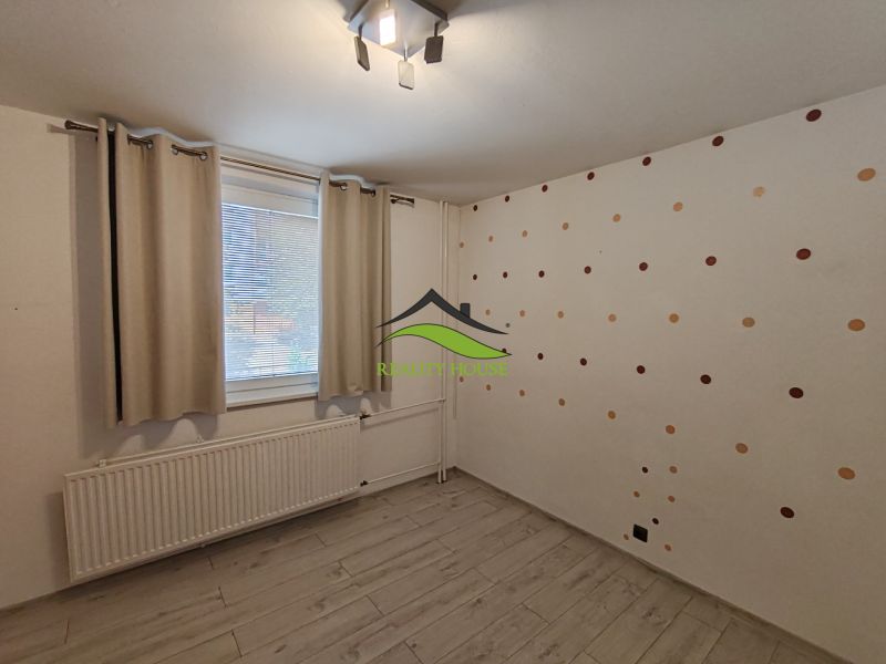 Pokoj ve 3-pokojovém bytě s podlahou s dřevěným dekorem a puntíkovanou tapetou.