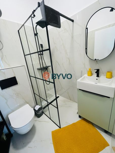 Koupelna v 2-pokojovém bytě se sprchovým koutem, závěsným WC a oranžovým koberečkem.
