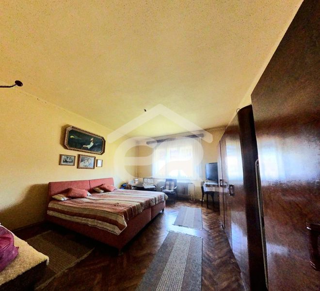 Ložnice v rodinném domě s podlahou s dřevěným dekorem, postel, skříně, obrazy na stěně.