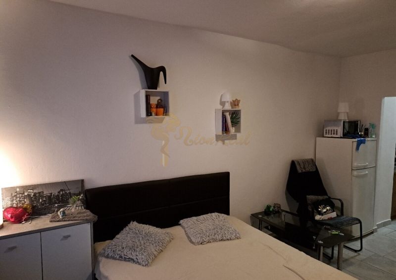 Garsonka s postelí, dekoracemi na stěně a křeslem vedle lednice.