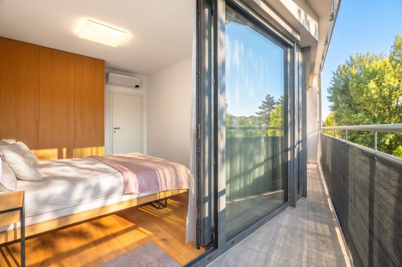 Ložnice s velkou skleněnou stěnou, podlahou s dřevěným dekorem a balkonem v 2pokojovém bytě.