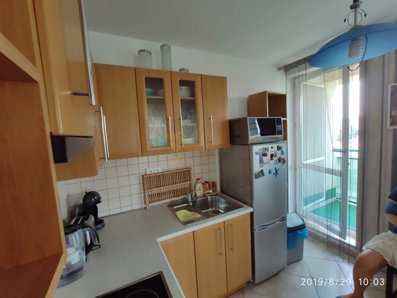Kuchyně s dřevěnými skříňkami, mikrovlnkou a lednicí v 2-pokojovém bytě.