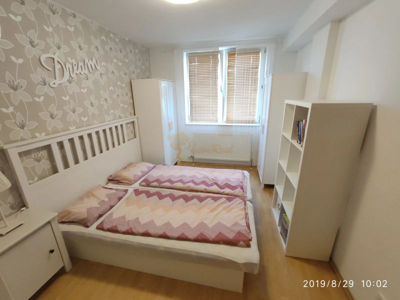 Ložnice s postelí, podlahou s dřevěným dekorem a květinovou tapetou v 2-pokojovém bytě.