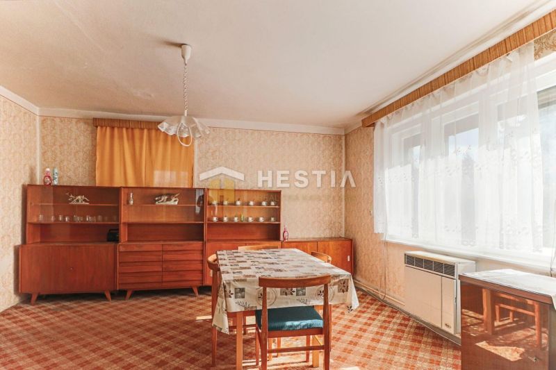 Interiér rodinného domu s jídelním stolem, starším nábytkem a kobercem.