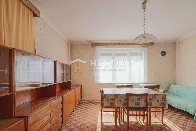Jídelna v rodinném domě s retro nábytkem a kobercem, dominuje světlé okno.