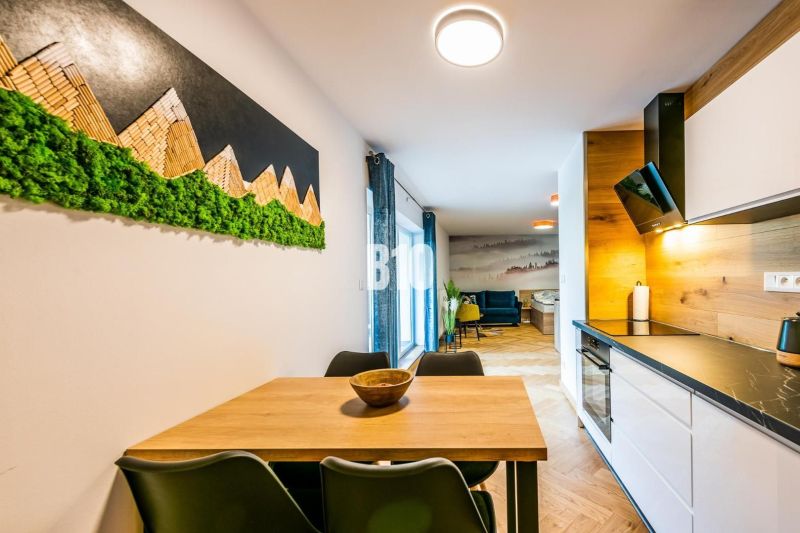 Interiér rekreačního apartmánu s kuchyňskou linkou a stolem, podlaha s dřevěným dekorem.