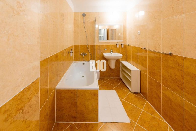 Koupelna v rekreačním apartmánu s vanou, umyvadlem a světlými obklady.