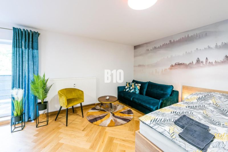 Stylový rekreační apartmán s podlahou s dřevěným dekorem, pohovkou a rostlinami.