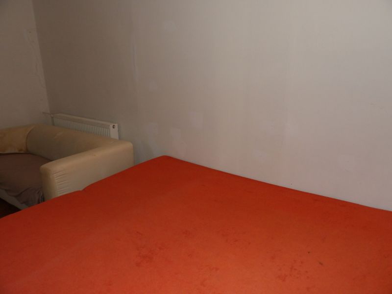 Pokoj s oranžovou postelí a béžovým křeslem v dvoupokojovém bytě.