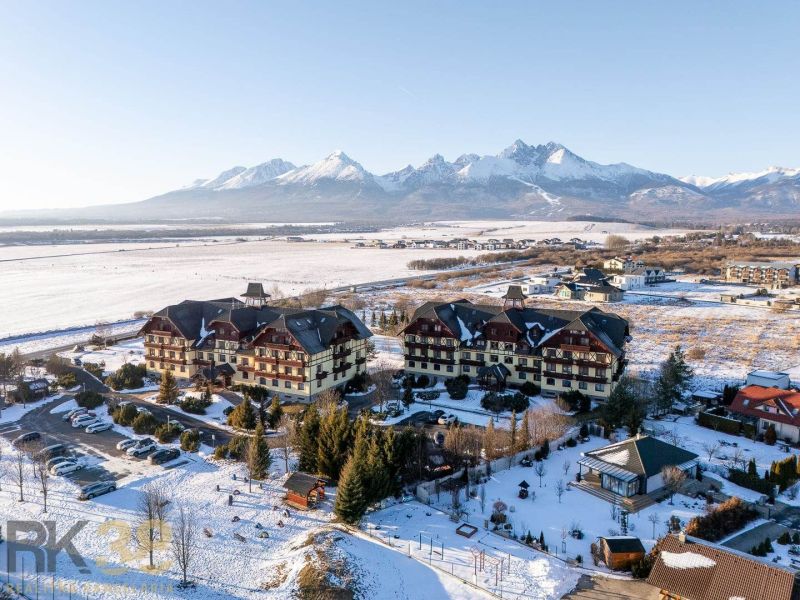 Zimní scenérie ve Velké Lomnici s výhledem na Tatry a budovy, nabízející 2-pokojové byty.