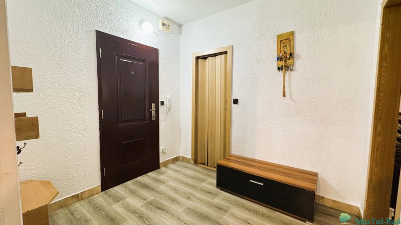 Interiér 4-pokojového bytu s bílými stěnami, podlahou s dřevěným dekorem a tmavými dveřmi.